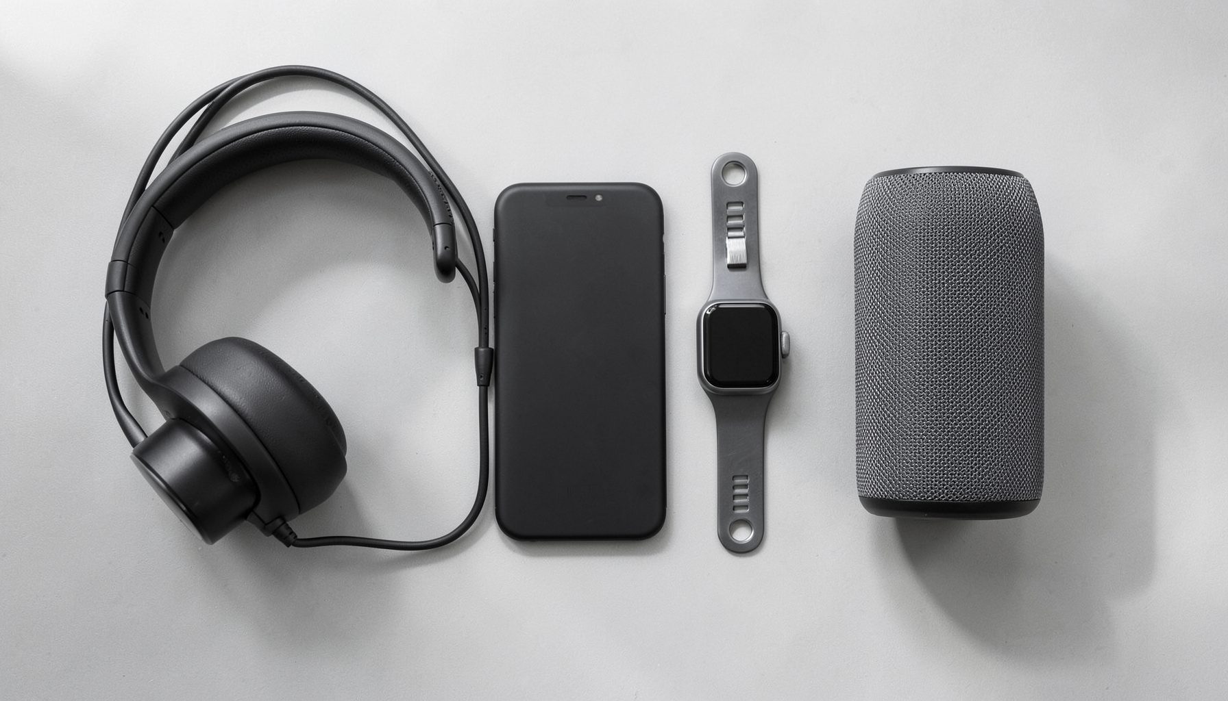 A clean flat-lay of modern consumer electronics on a light grey surface, including headphones, a smartphone, and a smartwatch